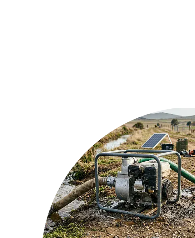 Portable engine-driven water pump on a muddy rural riverbank.