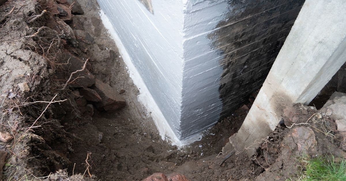 A brick foundation with surrounding soil excavated and a white waterproof coating applied to its surface.