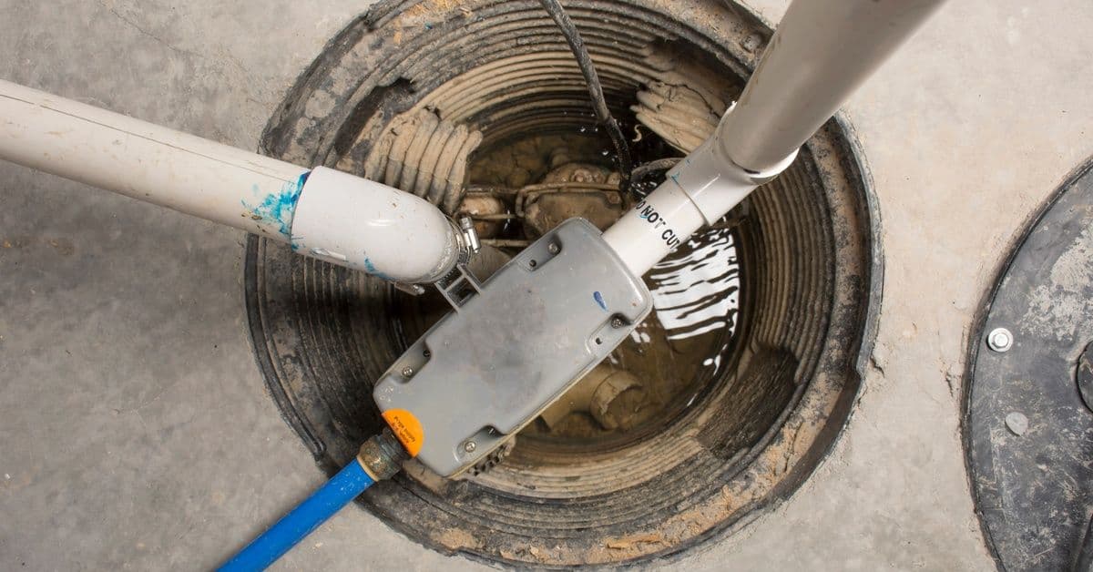 An overhead shot of an open sump pump set into a concrete floor, with several pipes emerging from the opening.