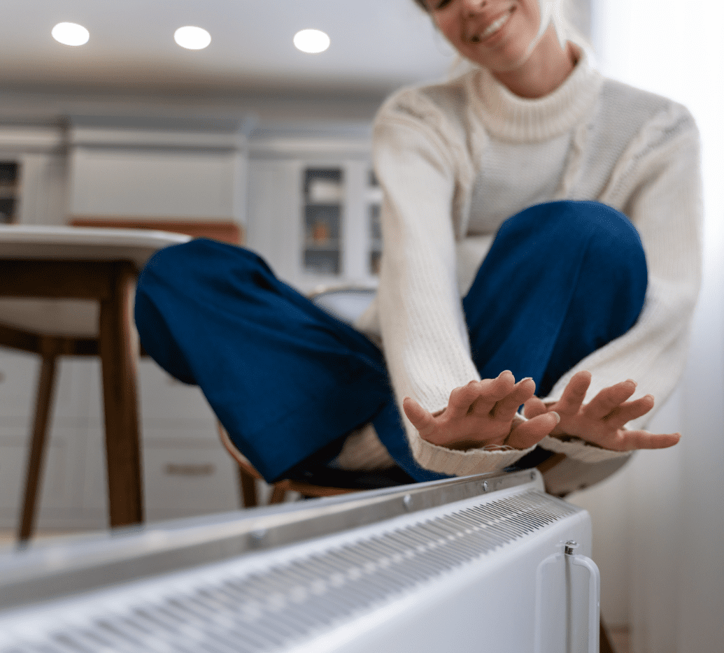 Woman warming her hands with a heater at home