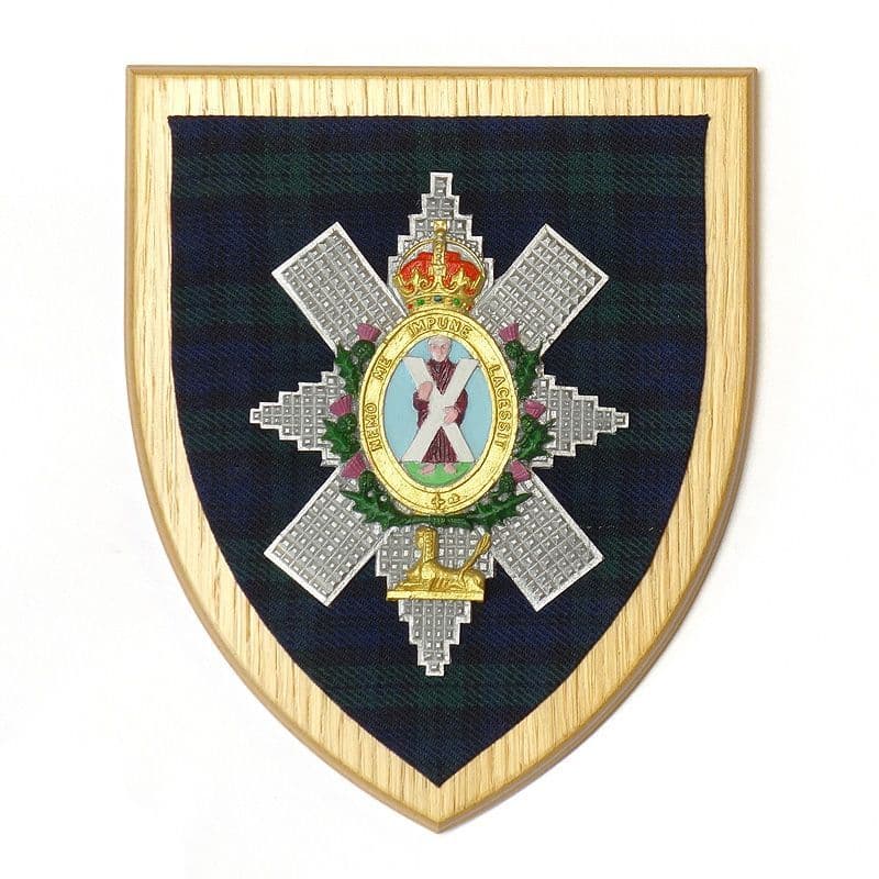 Metallic finished Black Watch cap badge set against the regimental tartan on a solid wooden