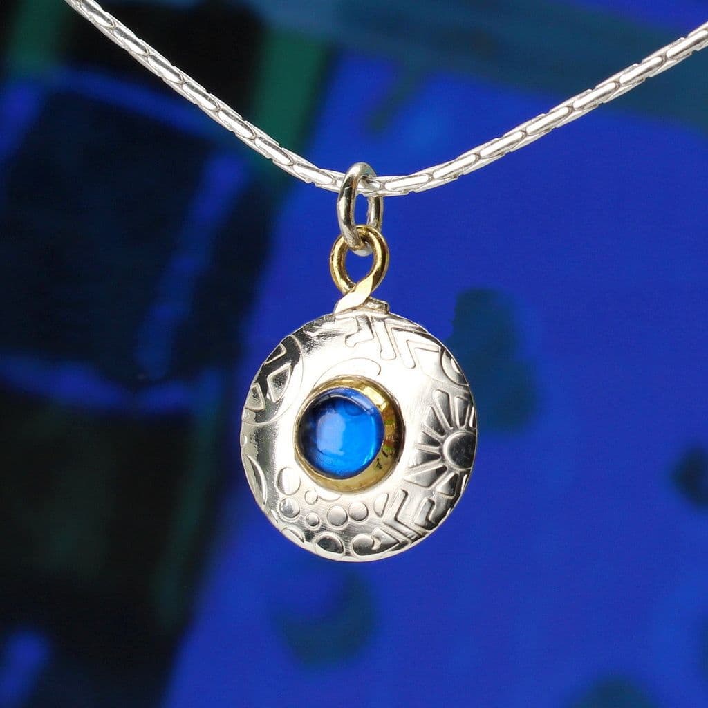 A sterling silver round pendant featuring a blue spinel gemstone and an embossed pattern. The pendant hangs on a quality sterling silver chain